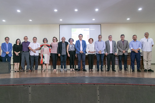 Imagem: De pé, no auditório da Faculdade de Direito, 15 pessoas, entre homens e mulheres, compõem a mesa solene do evento do Programa Educação em Tempo Integral. O reitor Custódio Almeida está ao centro. (Foto: Álvaro Graça Jr./ UFC Informa)