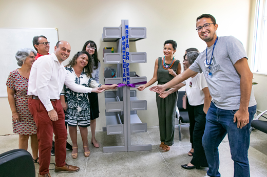 Imagem: Três homens e seis mulheres puxam juntos uma fita roxa para inaugurar a Prateleira Maria da Penha. (Foto: Álvaro Graça Jr./ UFC Informa)