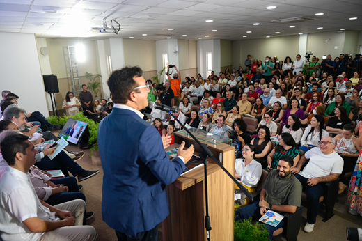 Imagem: Reitor Custódio Almeida aparece de costas, discursando no púlpito para o público do auditório