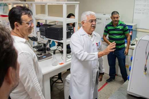 Imagem: professor mostrando uma máquina de uma laboratório ao reitor