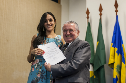 Imagem: Reitor Henry Campos entrega o termo de posse para a nova servidora Patrícia Araújo Silva, que leu o termo de compromisso na solenidade (Foto: Viktor Braga/UFC)