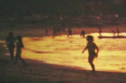 Imagem: Foto de orla durante pôr do sol, com pessoas andando na areia da praia