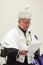 Imagem: Foto do Prof. Henry Campos segurando um papel e lendo ao microfone