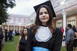 Imagem: foto de uma jovem vestida de beca nos jardins da Reitoria