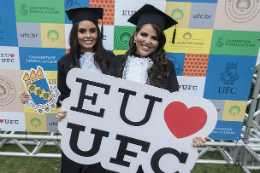 Imagem: Fotos de concludentes vestidas com beca segurando uma placa onde se lê "eu coração (amo) UFC"