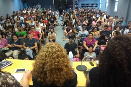 imagem: foto de auditório lotado com pessoas sentadas em cadeiras e no chão