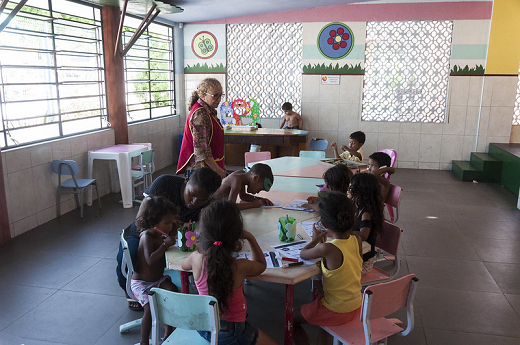 Imagem: Foto de crianças sentadas ao redor de uma mesa desenhando em papeis