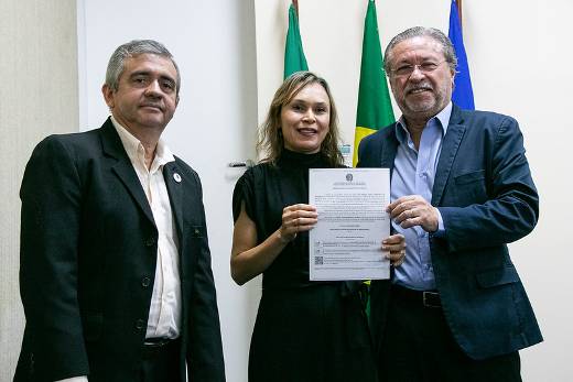 Imagem: três pessoas de preto posam para foto, sendo uma mulher ladeada por dois homens