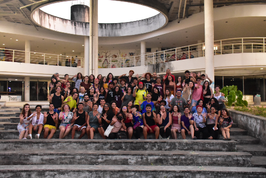 Imagem: Jovens aparecem sentados e em pé nos degraus de uma escada cinza posando para a foto. Todos estão com uma mão espalmada, fazendo referência à nota 5 do curso