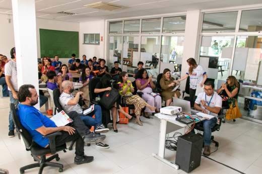 Imagem: Foto da sala do Thinkathon cheia de pessoas sentadas para assistir às apresentações em formato de pitch