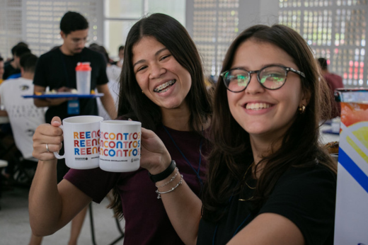 Imagem: Foto de duas alunas sorrindo e brindando com um copo de suco no Restaurante Universitário da UFC