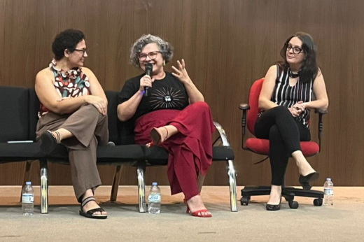 Imagem: Professora Diana (ao centro) e as duas participantes da mesa redonda, sentadas em cadeiras no palco