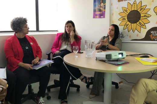 Imagem: Três mulheres, entre elas a vice-reitora e a deputada, sentadas em reunião, ao redor de uma mesa 