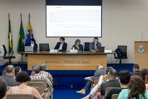 Imagem: Foto mostra o palco do auditório Martins Filho na Reitoria com a mesa onde estão sentados em cadeiras, da esquerda para a direita, a pró-reitora de Pesquisa e Pós-Graduação da UFC e relatora da proposta, Regina Célia Monteiro de Paula; o reitor Custódio Almeida; a vice-reitora Diana Azevedo; e o coordenador de Articulação Política institucional da UFC Daniel Fonsêca.