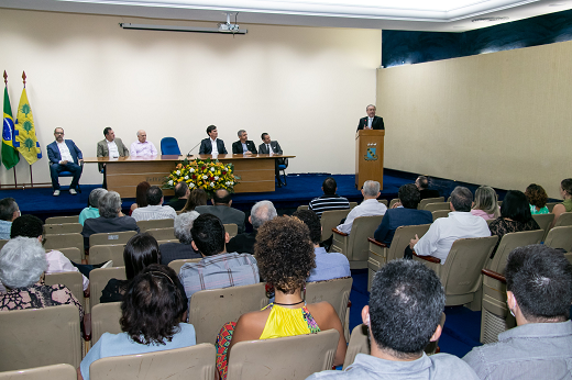 Imagem: Foto de solenidade no auditório da Reitoria mostra o reitor Cândido Albuquerque falando no púlpito (à direita); ao lado dele, estão sentados os membros da mesa e diante dele, o público, também sentado. (Foto: Marco Fukuda/ UFC Informa)