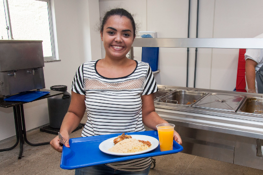 Imagem: estudante segura bandeja com prato de comida