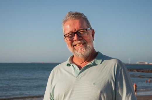 Imagem: foto homem com barba branca e blusa azul, com mar ao fundo