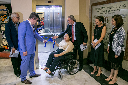 Imagem: Estudante Tamires Xavier (ao centro, em cadeira de rodas), desfaz a fita na inauguração do novo elevador da FADIR. Ao seu lado, estão o vice-reitor Glauco Lobo, o diretor da FADIR Maurício Benevides, o reitor Cândido Albuquerque, a vice-diretora da FADIR Camilla Freitas e a pró-reitora de Extensão, Elizabeth Daher. (Foto: Ribamar Neto/ UFC Informa)