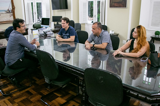 Imagem: Sentados à mesa, no Gabinete da Reitoria, o reitor Custódio Almeida (de costas, em primeiro plano) recebe o vereador Julio Brizzi e dois assessores, um homem e uma mulher. (Foto: Ribamar Neto/ UFC  Informa)