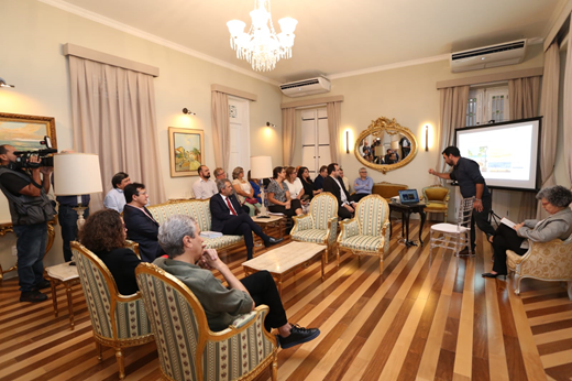 Imagem: Sentados no Salão Dourado, o governador Elmano de Freitas, o reitor e público formado por pró-reitores, assessores e secretários acompanham palestra do Prof. Marcelo Soares (de pé, com camisa azul escura) sobre a proposta de uma estação científica da UFC em Jericoacoara. Ele projeta slides em um data-show. (Foto: Arlindo Barreto)