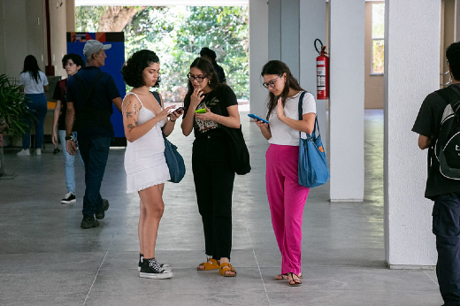 Imagem: três estudantes em pé olhando o celular