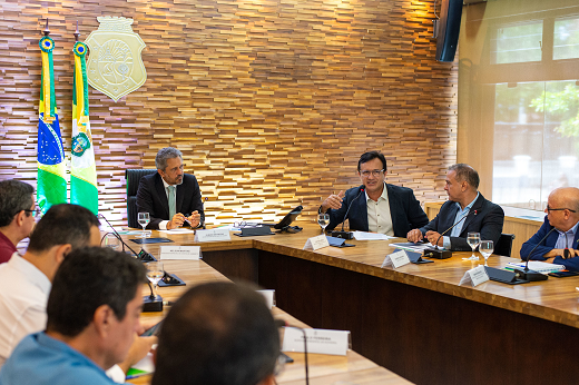 Imagem: Sentados à mesa, no Salão Oval do Palácio da Abolição, estão o governador Elmano de Freitas (de terno escuro, à cabeceira), ladeado pelo reitor Custódio Almeida (também de terno escuro) e por secretários, representantes de agências estaduais e acadêmicos. (Foto: Carlos Gibaja/ Casa Civil)