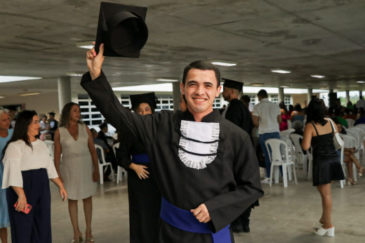 Imagem: formando Gilma Silva posa para foto segurando o chapéu da beca no ar