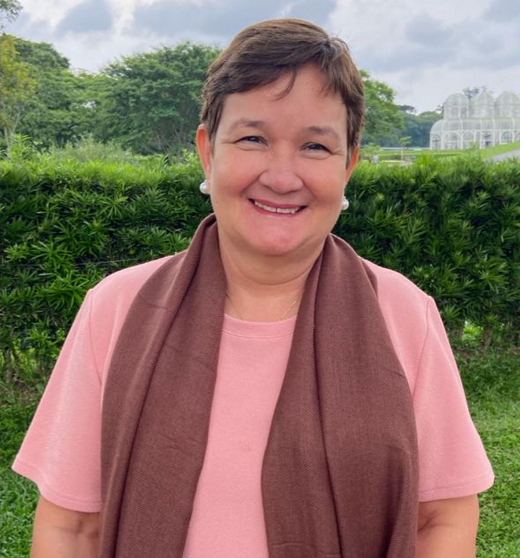 A professora Mônica Cavalcante. Mulher de meia idade, branca, com cabelo curto. Veste roupa rosa.