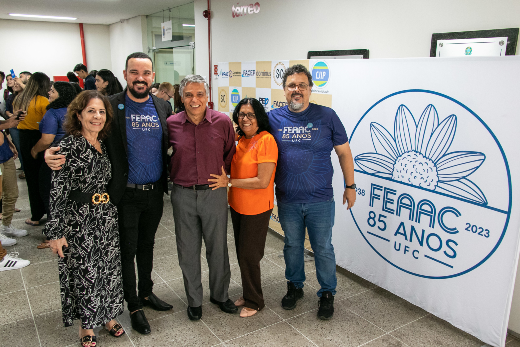 Imagem: grupo de pessoas reunido em pé ao lado de banner de fundi branco com a logo dos 85 anos da FEAAC