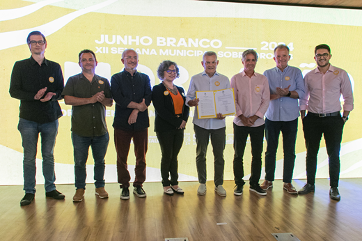 Imagem: Sete pessoas de pé no palco da solenidade; ao centro, a vice-reitora Diana Azevedo e o prefeito José Sarto, que segura o documento assinado. (Foto: Álvaro Graça Jr./ UFC Informa)