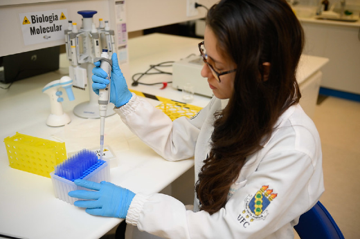 Imagem: menina jovem de óculos e cabelos longos manuseia instrumentos dentro de um laboratório