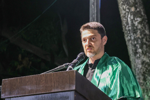 Imagem: homem de barba rala e grisalha e cabelo curto aparece trajando uma veste talar da cor verde, atrás de um púlpito e falando ao microfone